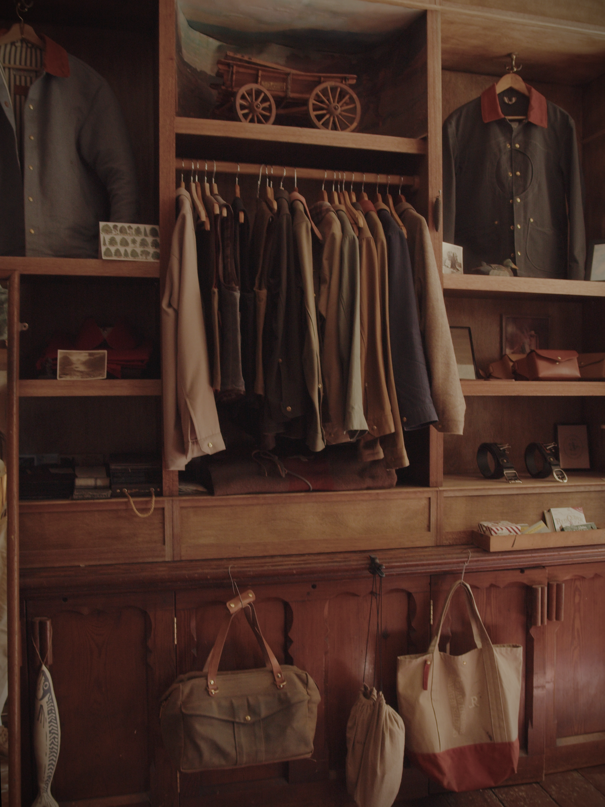 Workshop cabinet with jackets on display and on the rail, alongside belts, bags, and decorative objects.